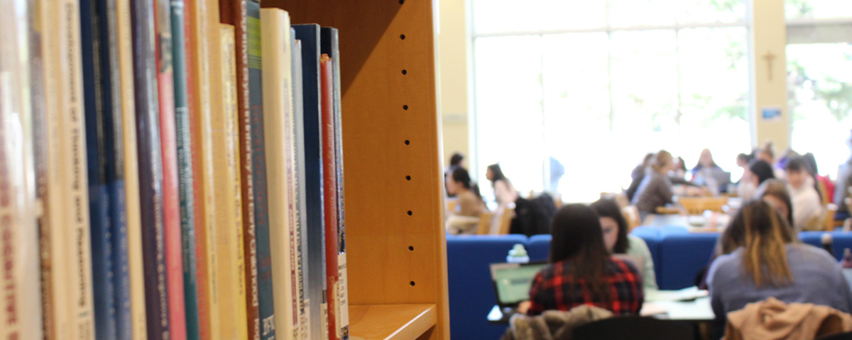 A shelf of library books, with students studying in the background